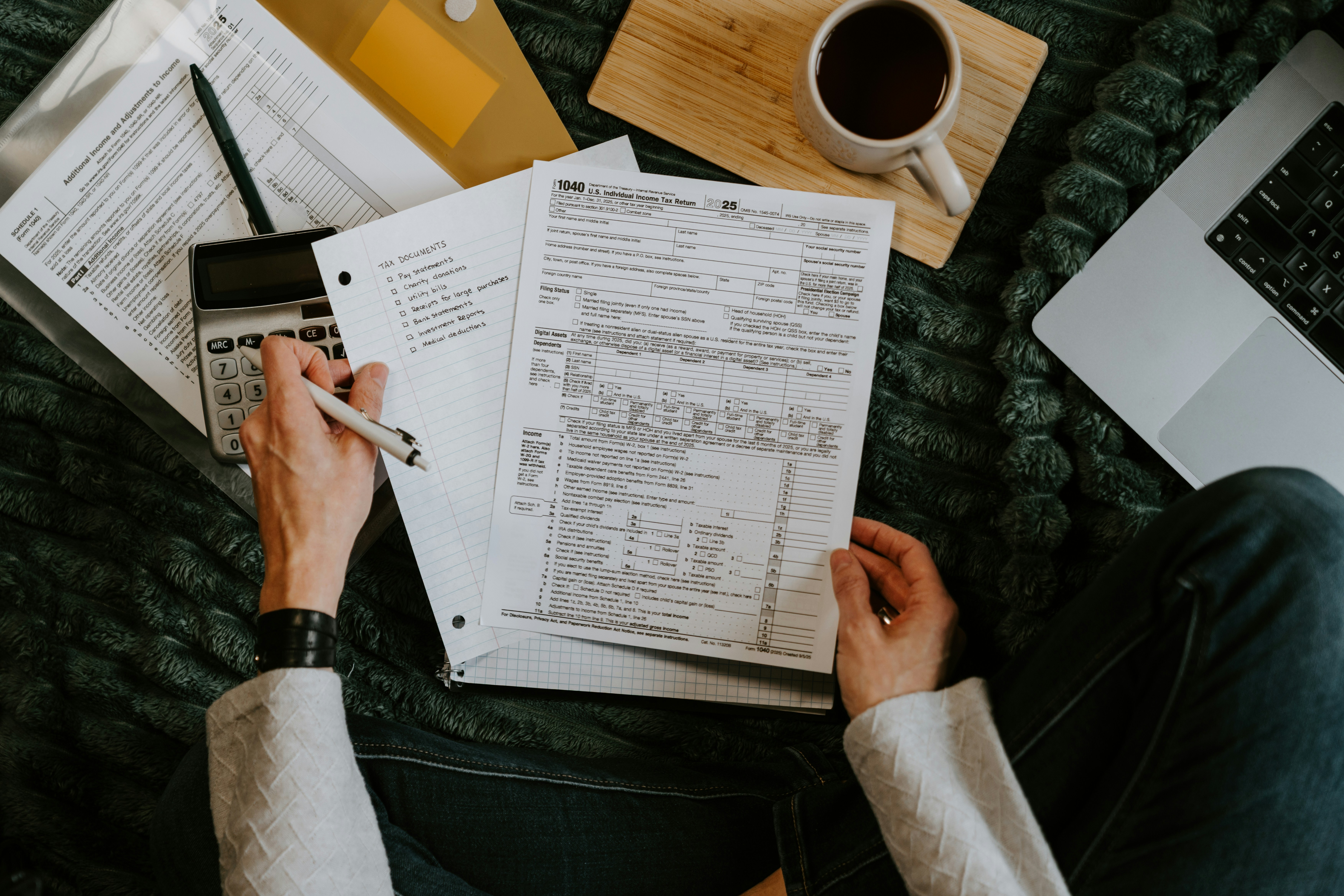 Person reviewing documents with calculator and laptop.